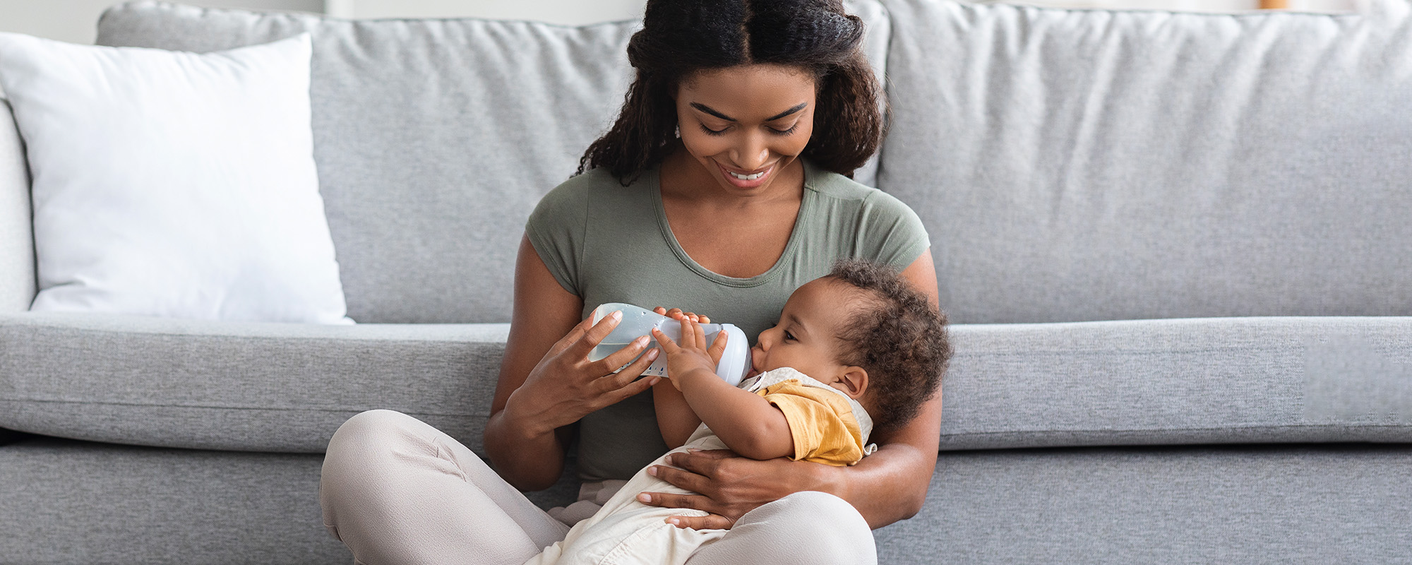 maternity leave concept. young black mother giving bottle with water to baby